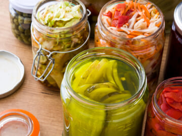 Overhead shot of colorful fermented preserved vegetables in jars on a wooden table.