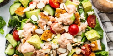 A salad with chicken, tomatoes, avocado and dressing on a plate.