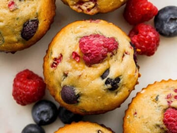 A group of muffins with raspberries and blueberries.