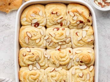 Freshly baked almond-topped sweet rolls in a white baking dish.