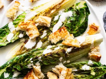 Grilled romaine lettuce with croutons and drizzled dressing on a plate.