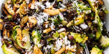 A bowl of brussels sprout salad with nuts and raisins.