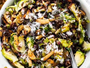 A bowl of brussels sprout salad with nuts and raisins.