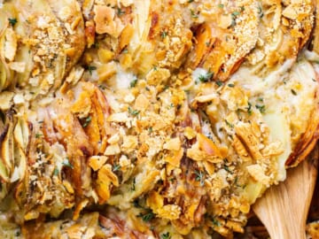 A dish of potato casserole with toppings and a wooden spoon.