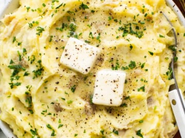 A bowl of mashed potatoes with cheese and herbs.