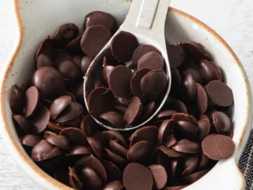 Chocolate chips in a white bowl with a spoon.