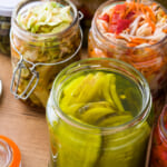 Overhead shot of colorful fermented preserved vegetables in jars on a wooden table.