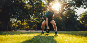 Full length portrait of fit young man training with kettlebell in the park.