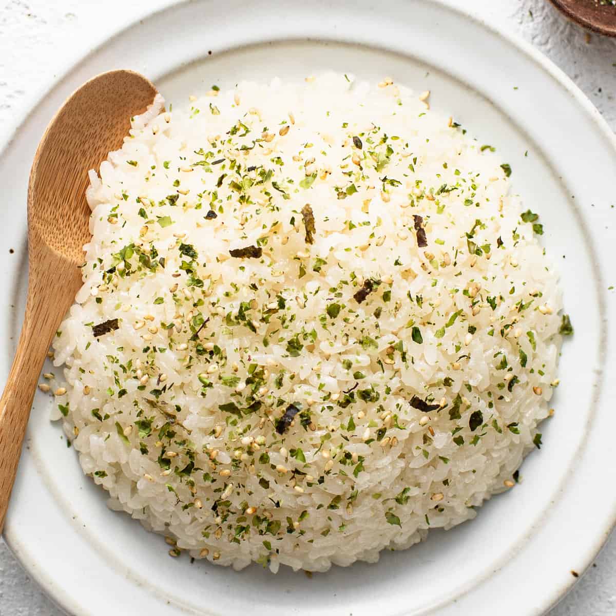 Japanese rice on a white plate with a wooden spoon.