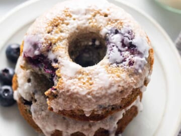 A stack of blueberry glazed donuts on a plate.