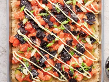 A pizza with salmon, avocado, and arugula on a baking sheet.