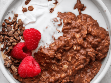 A bowl of chocolate protein oatmeal with raspberries and whipped cream.