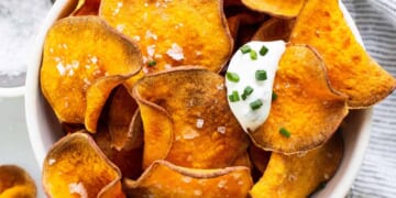 Sweet potato chips in a bowl with sour cream and parsley.