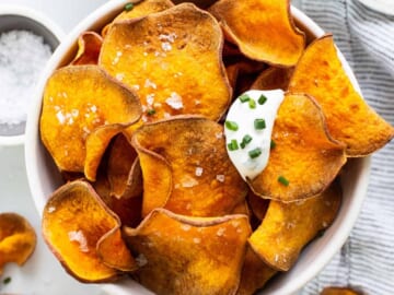 Sweet potato chips in a bowl with sour cream and parsley.