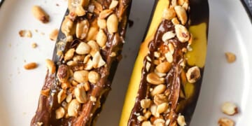 Two bananas with peanuts and chocolate on a plate.