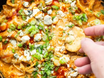 A person dipping chips into a bowl of buffalo chicken dip.