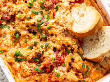 A casserole dish with chicken, tomatoes and bread.