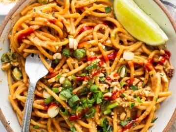 Thai peanut noodles in a bowl with lime and peanuts.