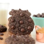 Flourless Double Chocolate Peanut Butter Cookies displayed on a cutting board accompanied by a glass of milk.