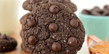 Flourless Double Chocolate Peanut Butter Cookies displayed on a cutting board accompanied by a glass of milk.