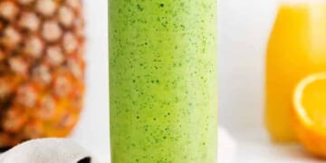 A green spinach smoothie in a glass with oranges and pineapples.