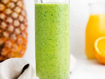 A green spinach smoothie in a glass with oranges and pineapples.