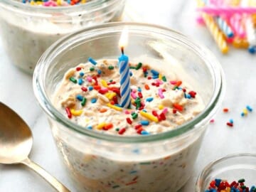 A birthday cake in a jar with sprinkles and a candle made from cake batter overnight oats.