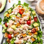 A salad with chicken, tomatoes, avocado and dressing on a plate.