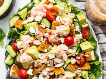A salad with chicken, tomatoes, avocado and dressing on a plate.