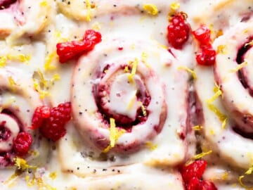 A plate of cinnamon rolls with raspberries and lemon.