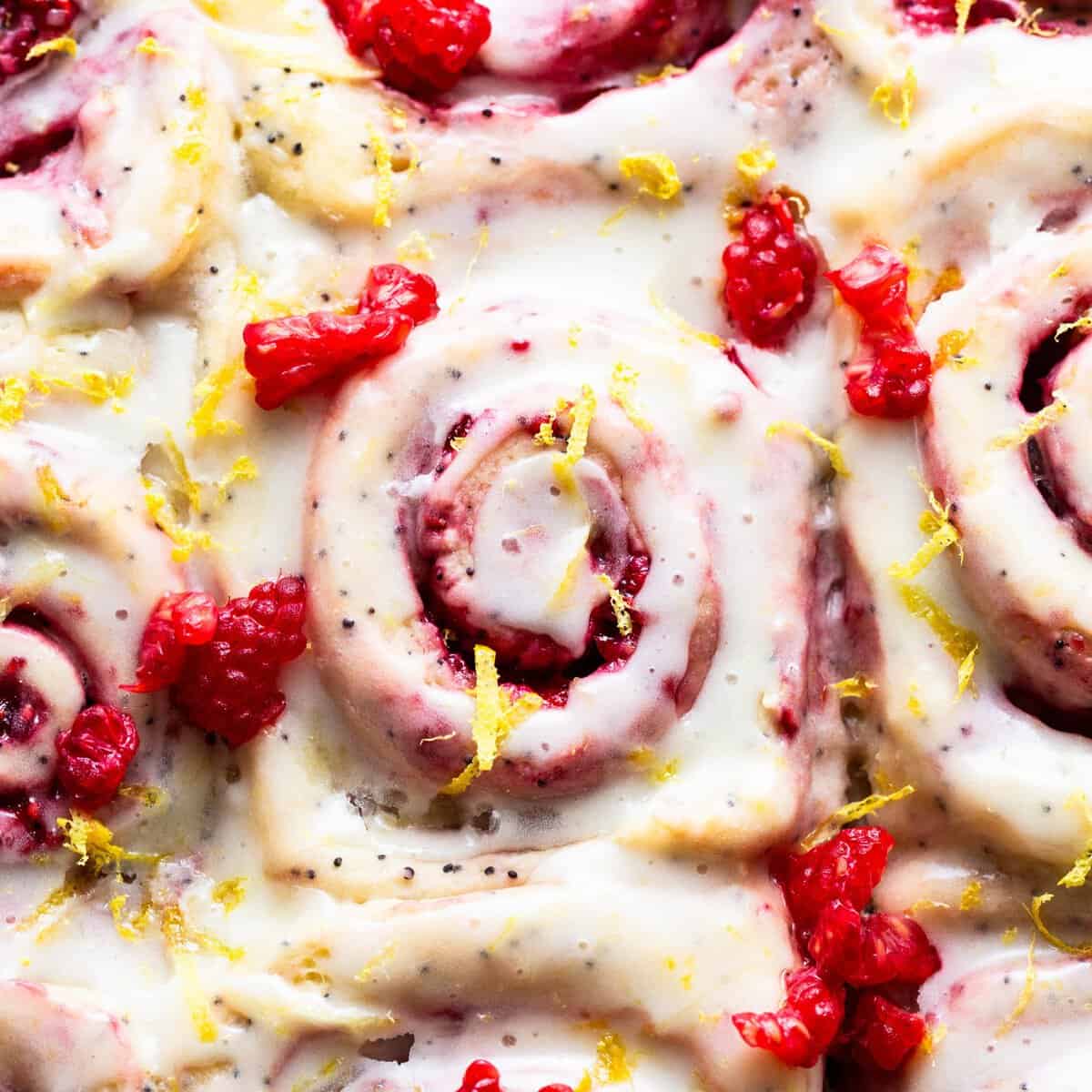 A plate of cinnamon rolls with raspberries and lemon.