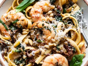 A bowl of pasta with shrimp and spinach.