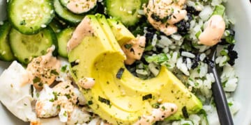 A white bowl with rice, cucumbers and avocado.