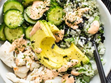 A white bowl with rice, cucumbers and avocado.