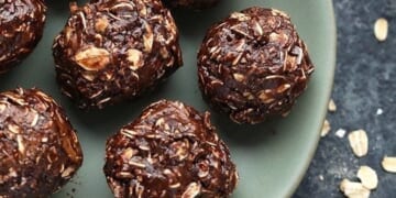 Cocoa oat balls decorated with peanut butter, placed on a plate alongside a bowl of oats.