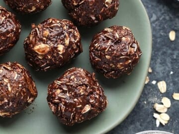 Cocoa oat balls decorated with peanut butter, placed on a plate alongside a bowl of oats.