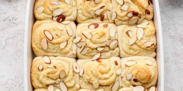 Freshly baked almond-topped sweet rolls in a white baking dish.