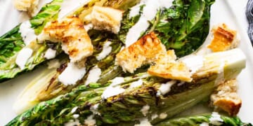 Grilled romaine lettuce with croutons and drizzled dressing on a plate.